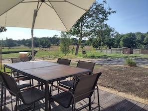 An outdoor dining area with a table and chairs under a large umbrella, overlooking a fenced pasture with trees and a clear sky. - The Charming Sicarderie Guesthouse, 30 minutes from Bordeaux (Peujard)