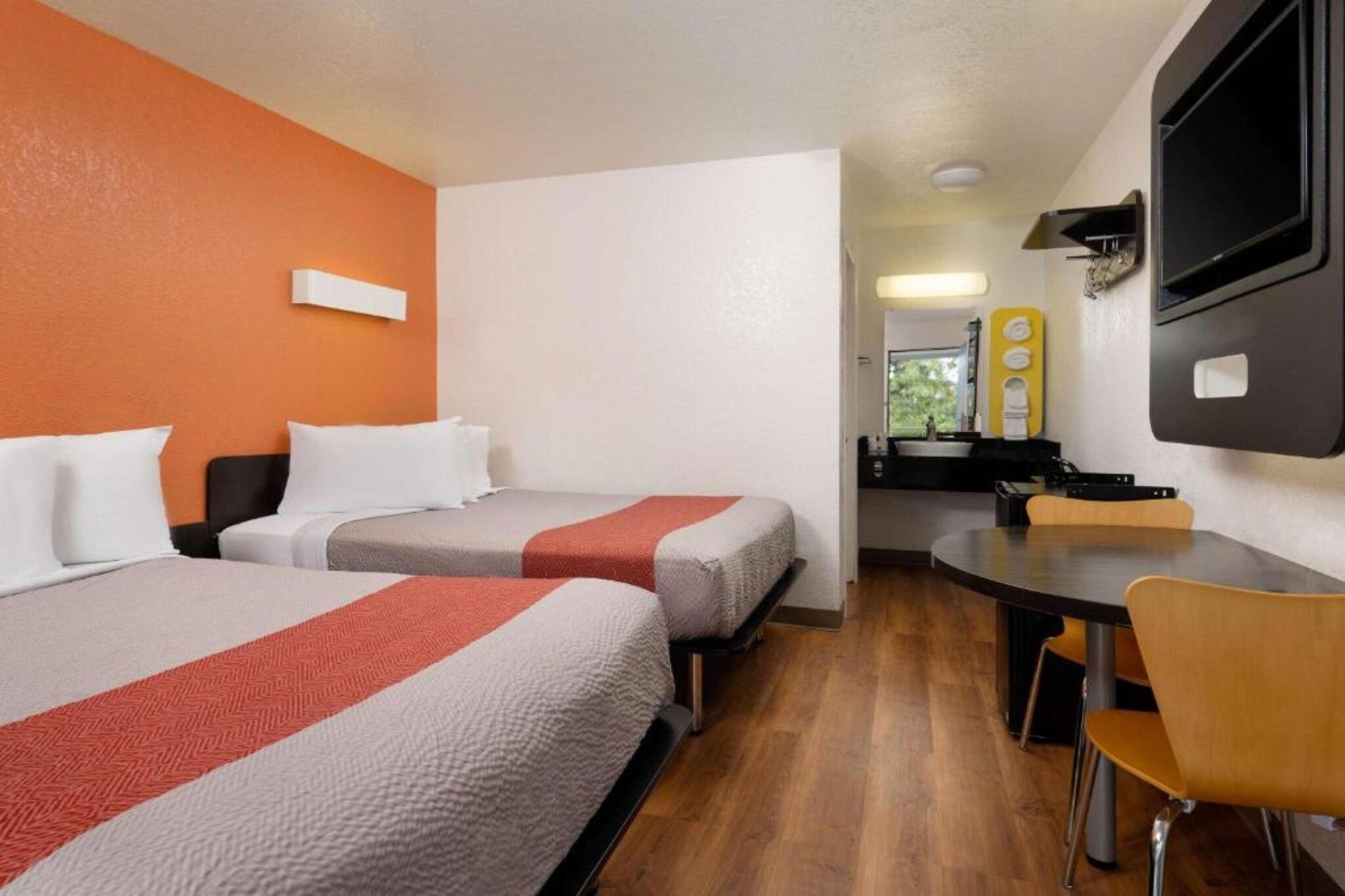 A hotel room with two beds, a small table, and a chair.