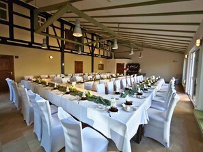 Une salle de banquet avec de longues tables dressées pour un événement formel, agrémentée de nappes et de chaises blanches.