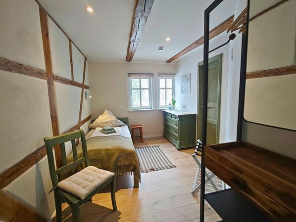 A bedroom with a bed, a chair, a dresser, and a window. - defaultName (Werdau)