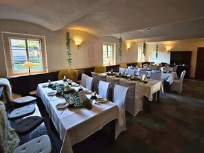 A dining area with multiple tables set for a meal, chairs, and a view of the outdoors through large windows. - defaultName (Werdau)