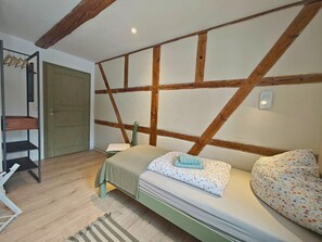 A room with a bed, wooden beams on the ceiling, a door, and a shelf. - defaultName (Werdau)