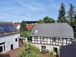 A traditional half-timbered building with a sloped roof, a visible garage, and a small garden area with potted plants. - defaultName (Werdau)