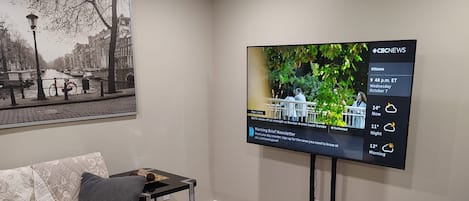 A modern living room with a flat-screen TV mounted on the wall, a sofa, a coffee table, and a dining table with chairs.