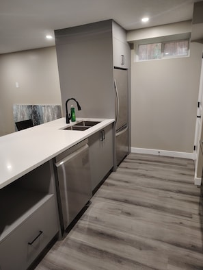 A modern kitchen with a stainless steel refrigerator, a white countertop, and a wooden floor. - Cozy 3-Bedroom House Rental in Calgary's Rosscarrock Area (Calgary)