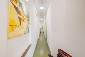 A corridor with a green floor, white walls, and a large abstract painting on the left. - Laoxao Memories (Đà Nẵng)