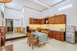 A modern kitchen with wooden cabinets, a dining table with chairs, and a refrigerator. - Laoxao Memories (Đà Nẵng)
