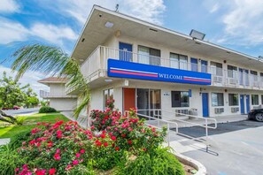 A hotel with a 'WELCOME' sign, a parking lot, and a garden with pink flowers. - 2 Full Beds | Non-Smoking (Bakersfield)