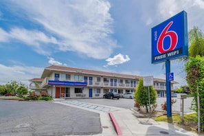 A motel with a blue sign indicating free wifi, a wheelchair accessible entrance, and a parking lot. - 1 Queen Bed | Non-Smoking (Bakersfield)