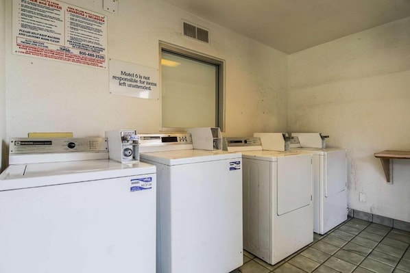 A laundry room with a row of washers and dryers, a sign indicating the room is not for unattended items, and a mirror above the dryers. - 1 Queen Bed | Non-Smoking (Bakersfield)
