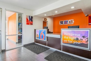 A hotel reception area with a glass door entrance, a reception desk, and a wall with a large number '6' sign. - 1 Queen Bed | Smoking (Bakersfield)