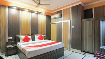 A hotel room with a bed, bedside tables, a wardrobe, an air conditioning unit, and a ceiling fan.