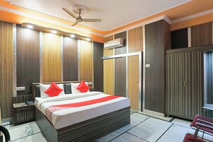 A hotel room with a bed, bedside tables, a wardrobe, an air conditioning unit, and a ceiling fan.