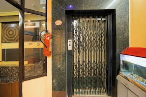 Un ascensor con una puerta metálica, un extintor de incendios en la pared y un acuario a la derecha.
