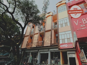 Un edificio de varios pisos con balcones, un letrero destacado que dice 'OYO Recommended' y un escaparate visible con señalización en un idioma extranjero.