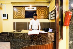 A reception desk with a man writing at it, a 'RECEPTION' sign above, and a 'No Smoking' sign on the wall.