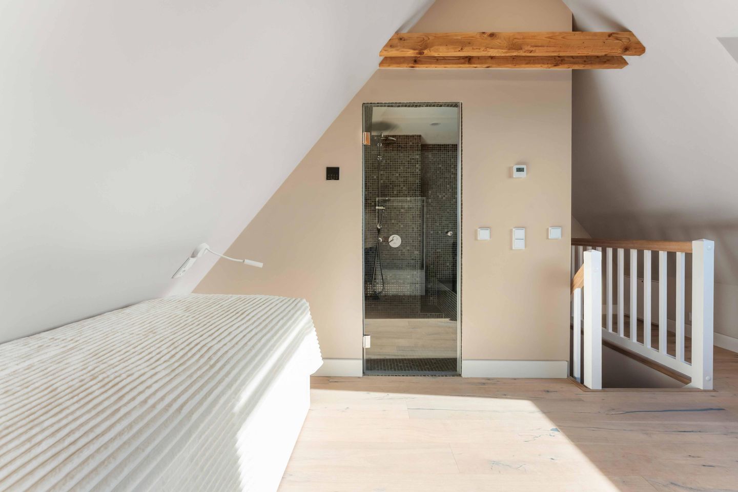 Une chambre avec un plafond en pente, un lit, une poutre en bois au plafond et une vue sur une salle de bain avec douche.