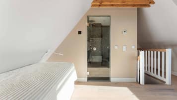 Une chambre avec un plafond en pente, un lit, une poutre en bois au plafond et une vue sur une salle de bain avec douche.