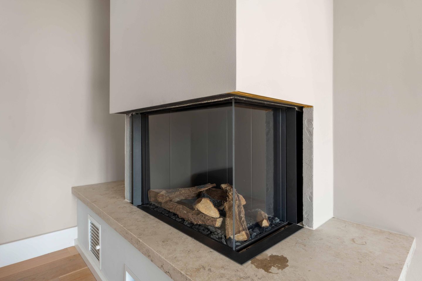 A corner fireplace with a glass enclosure, a stone base, and a visible fire.