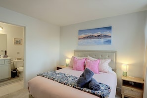 A bedroom with a bed, a nightstand, a painting, and a bathroom visible in the background. - Leos Cozy Getaway near SLC Airport & Downtown (Salt Lake City)