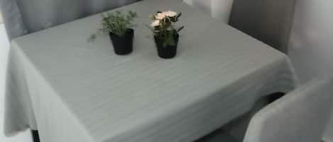 A dining table with a light green tablecloth, two potted plants, and a grey upholstered chair.
