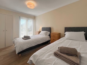 Ett hotellrum med två sängar, ett fönster med persienner, ett sängbord med en lampa och en garderob.