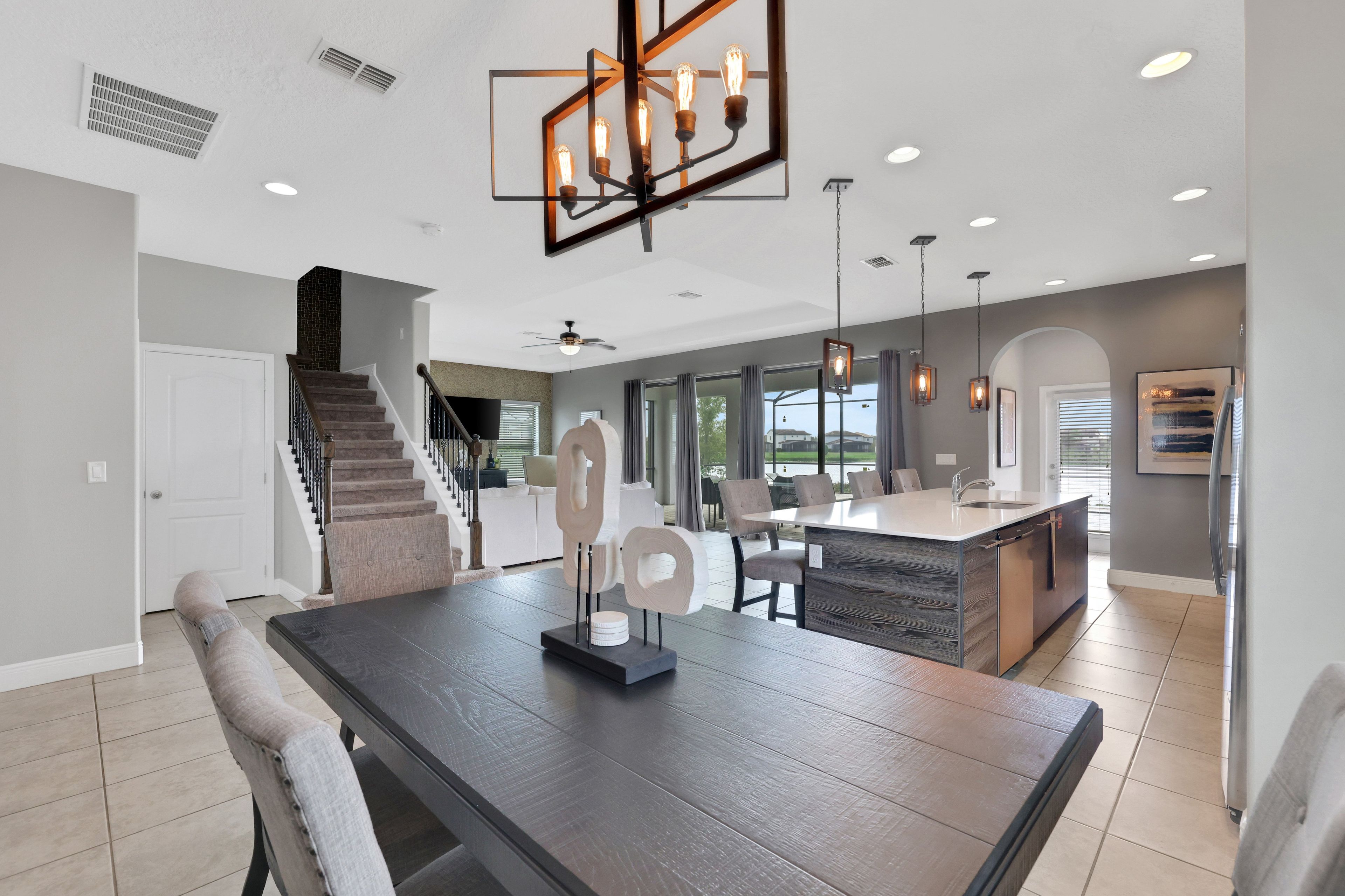 A modern kitchen with a central island, a dining area with a dark wooden table, and a staircase leading to another level.