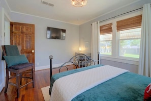A bedroom with a bed, a chair, a television on the wall, and a window with blinds. - Big Spring 'Bison House' w/ Patio & Yard! (Big Spring)