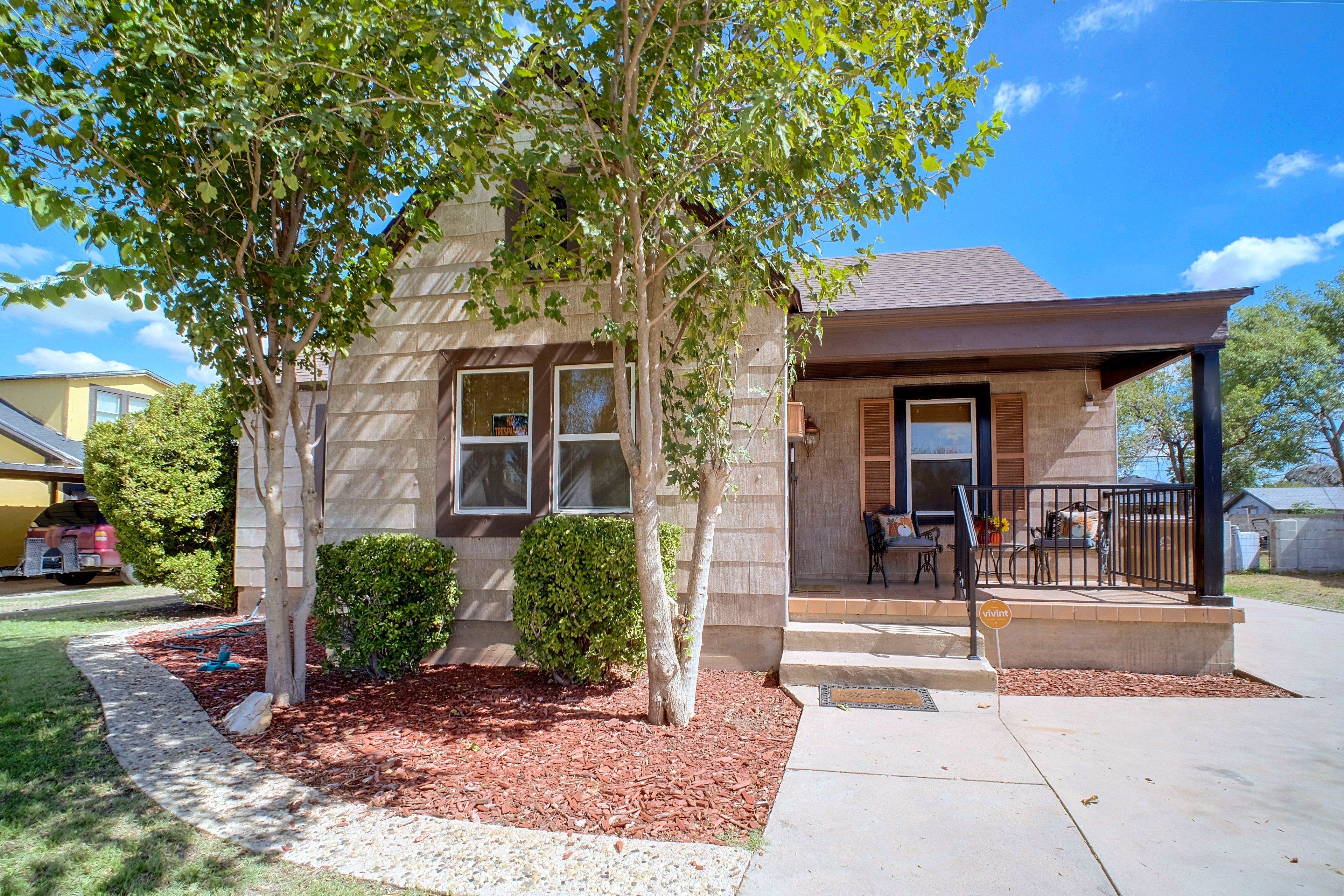 A single-story house with a front porch, a small garden area with mulch, and a clear blue sky.