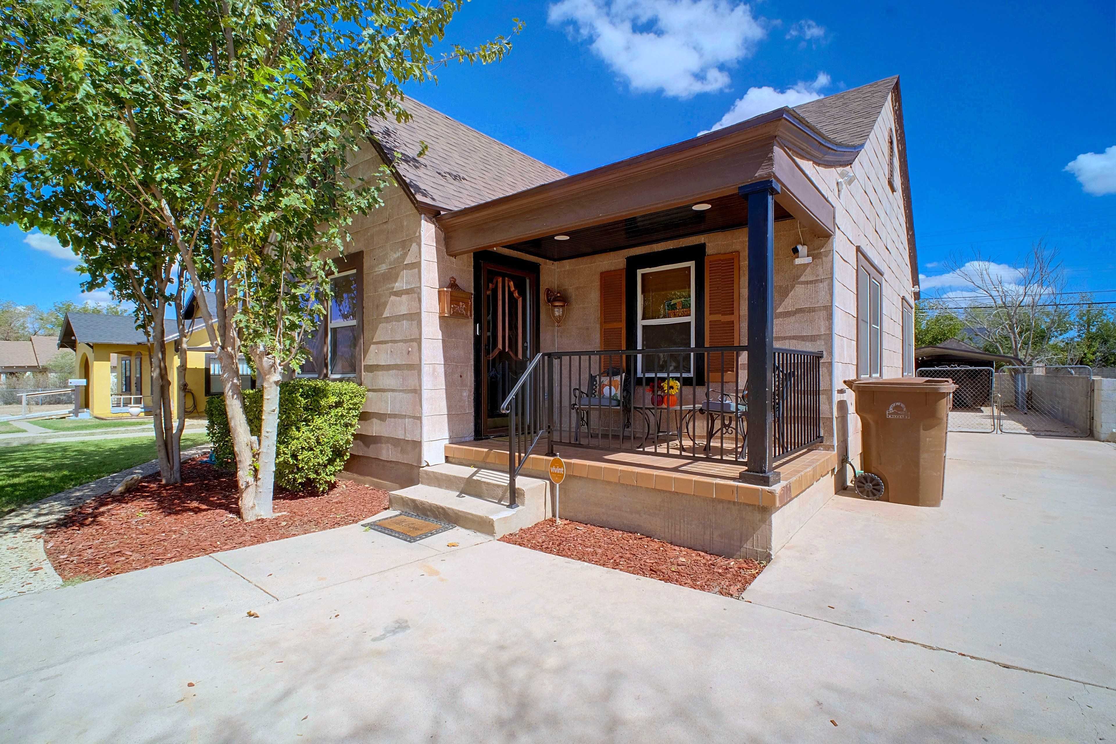 A two-story house with a front porch, a staircase leading to the entrance, and a small garden area with mulch and a tree.