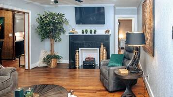 A living room with a fireplace, a ceiling fan, and a television mounted on the wall.