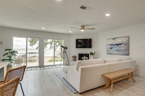 A modern living room with a sofa, a wooden bench, a telescope, and a TV mounted on the wall. - Putt, Play & Splash! Cedar Creek Lake Getaway (Gun Barrel City)