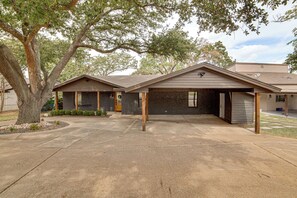 A two-story building with a garage, a covered porch, and a large tree in front. - Putt, Play & Splash! Cedar Creek Lake Getaway (Gun Barrel City)