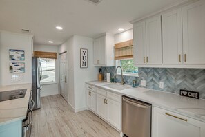 A modern kitchen with white cabinetry, a stainless steel dishwasher, and a herringbone tile backsplash. - Putt, Play & Splash! Cedar Creek Lake Getaway (Gun Barrel City)