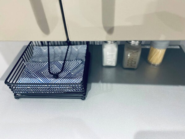 Un panier noir en fil métallique orné d’un motif géométrique, posé sur une surface blanche.