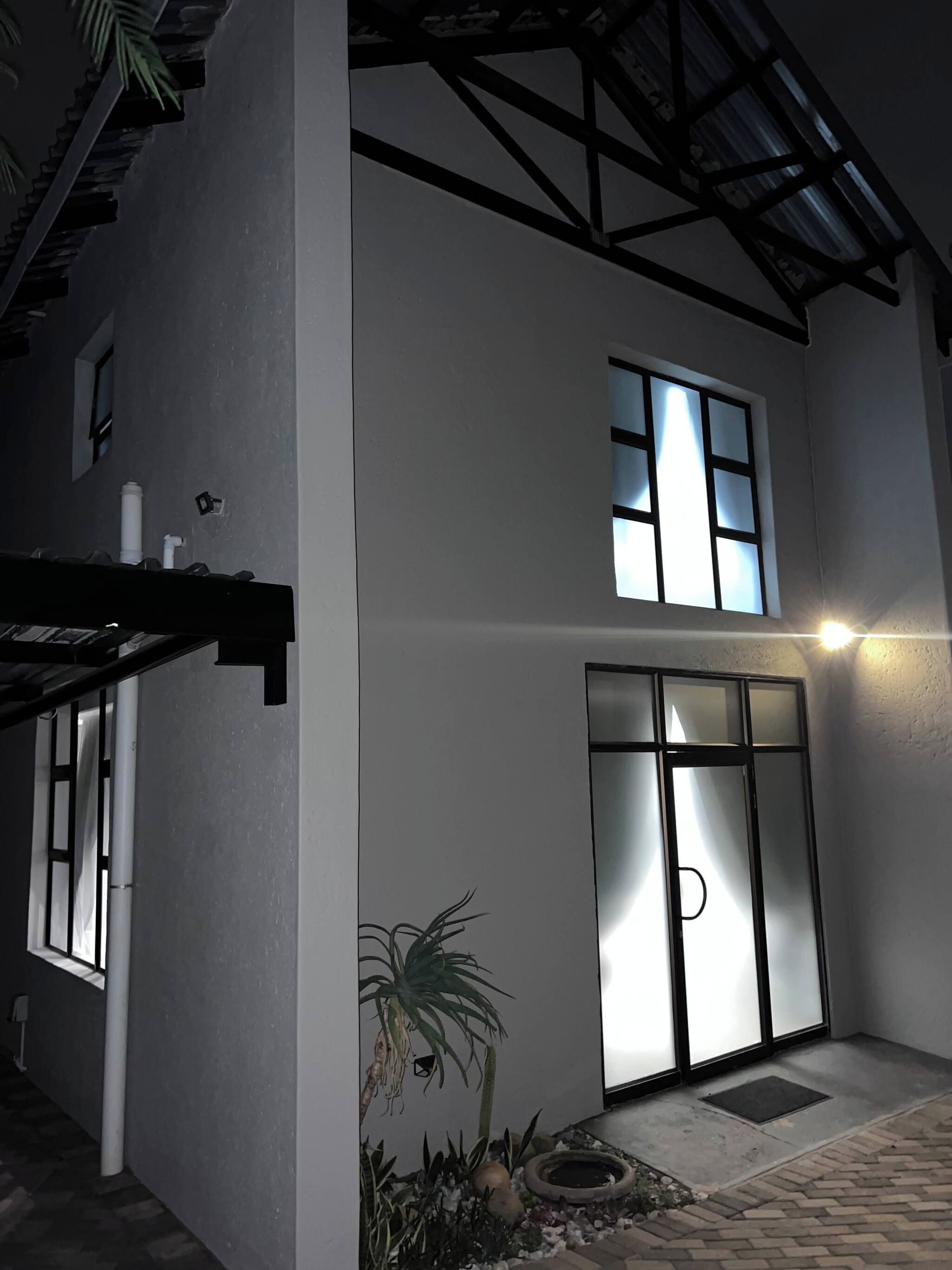 A two-story building with a large glass door entrance, a small garden with a palm tree, and a metal roof structure.