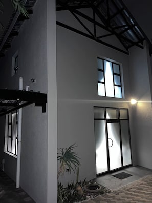 A two-story building with a large glass door entrance, a small garden with a palm tree, and a metal roof structure.