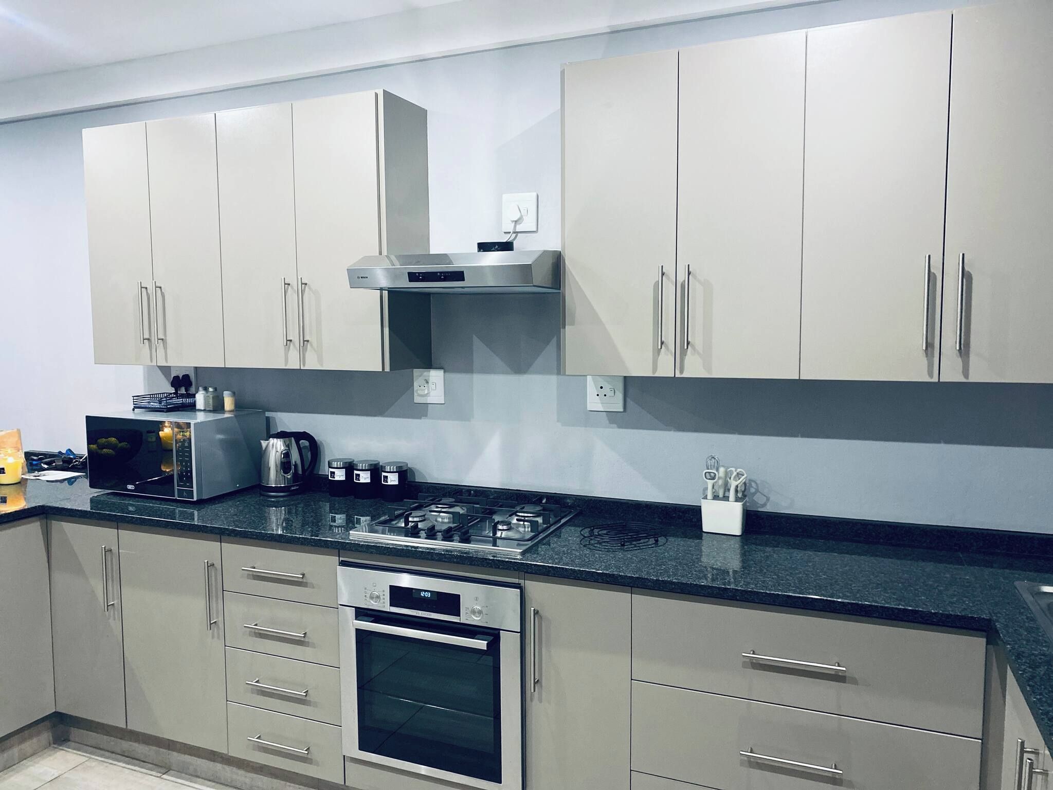 Een moderne keuken met roestvrijstalen apparatuur, grijze kastjes en een zwart aanrecht.