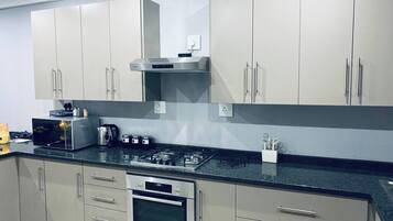 Een moderne keuken met roestvrijstalen apparatuur, grijze kastjes en een zwart aanrecht.