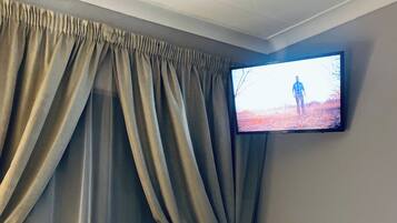 Een hotelkamer met een bed, een aan de muur bevestigde televisie en een raam met gordijnen.