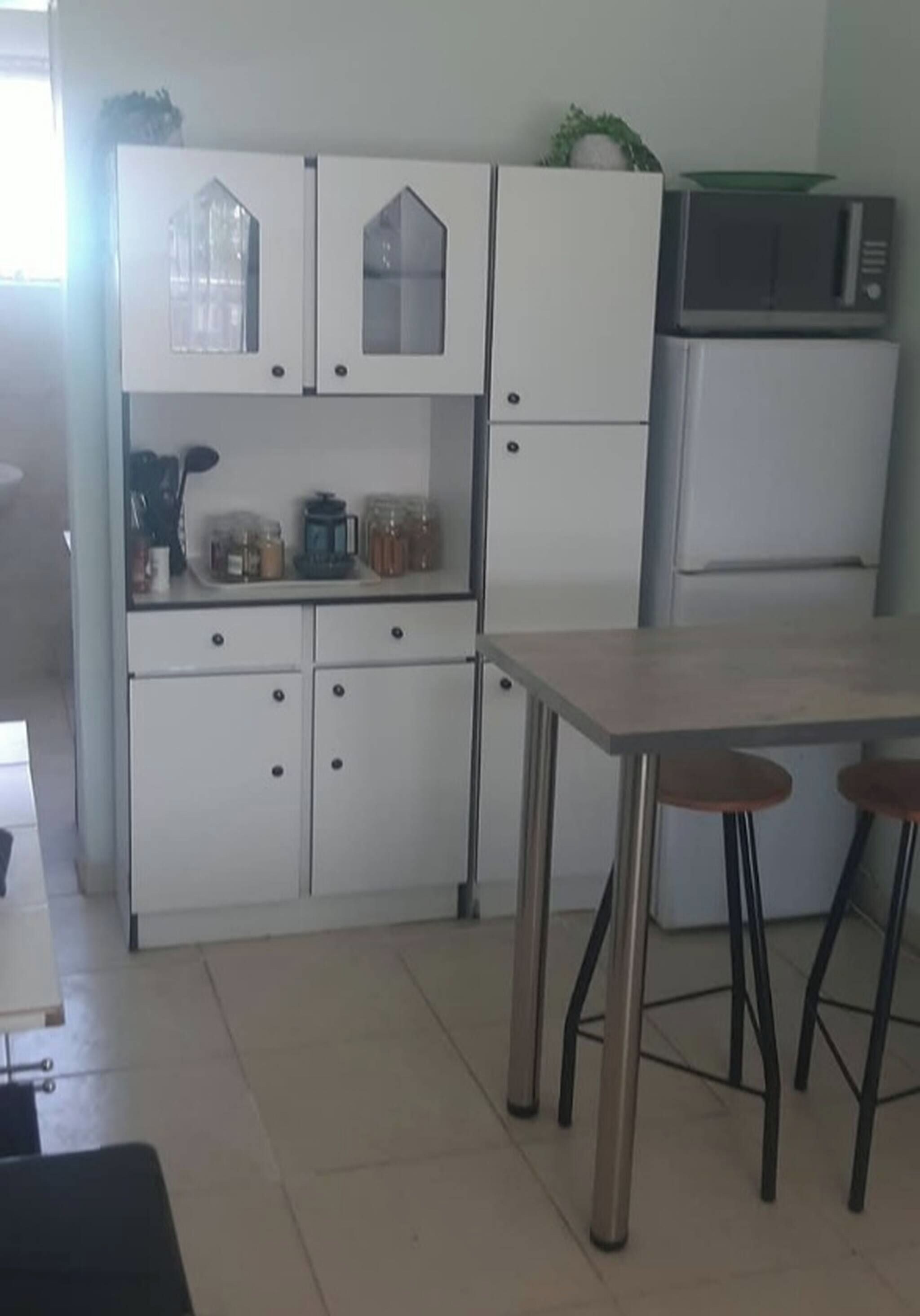 Una cocina con armarios blancos, un refrigerador, un microondas y una mesa con taburetes.