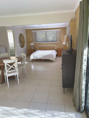 Ein Schlafzimmer mit einem Bett, einem Schreibtisch, einem Stuhl, einem Spiegel und einem Fenster mit Jalousien.