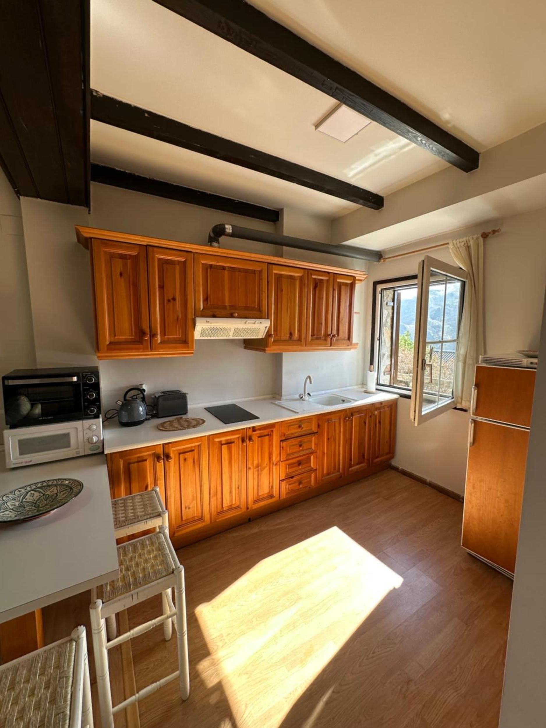 Cocina con gabinetes de madera, microondas, hervidor de agua, pileta y ventana con vistas.
