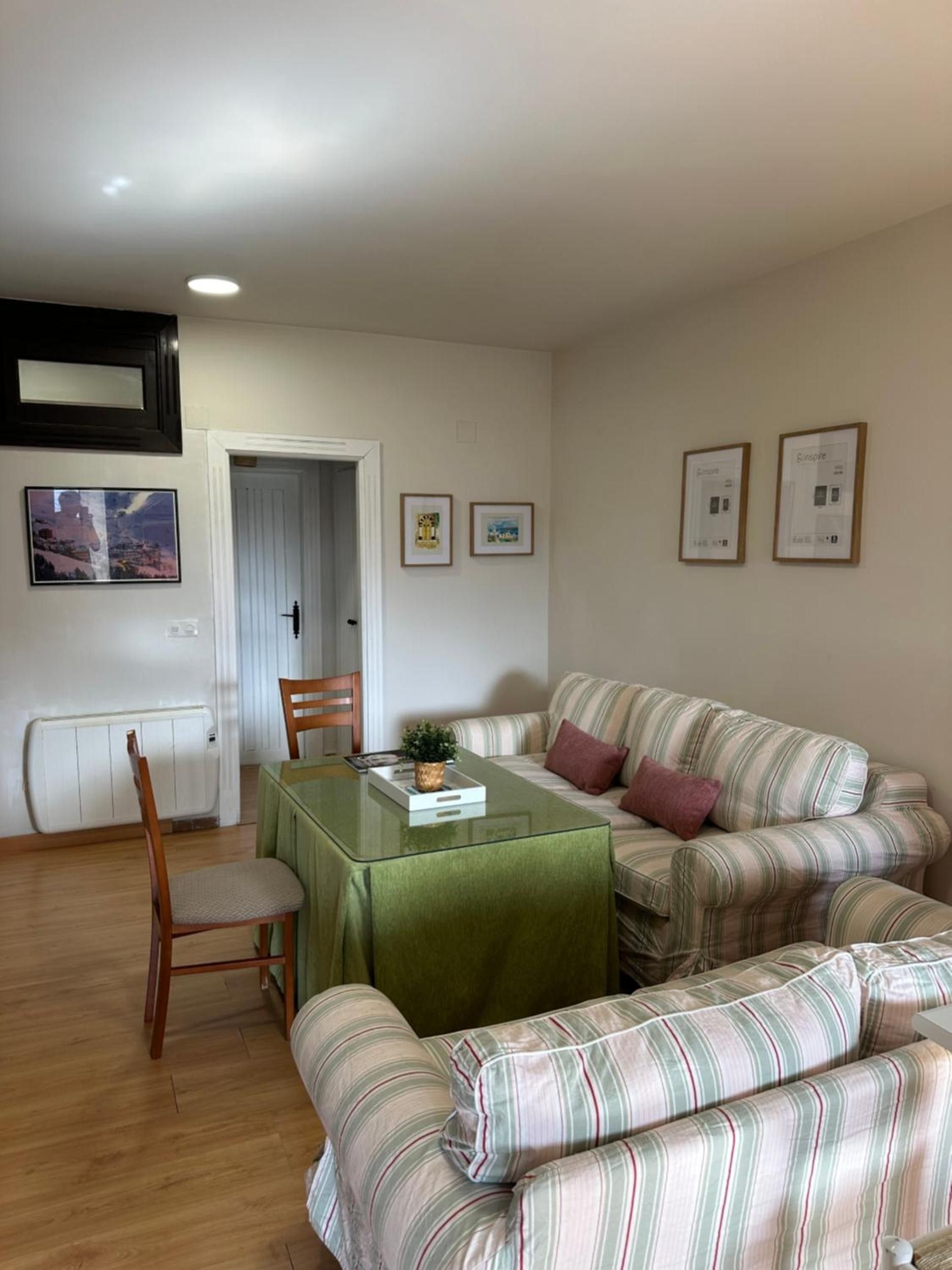 Una sala de estar con un sofá a rayas, una mesa de comedor con mantel verde y cuadros en la pared.