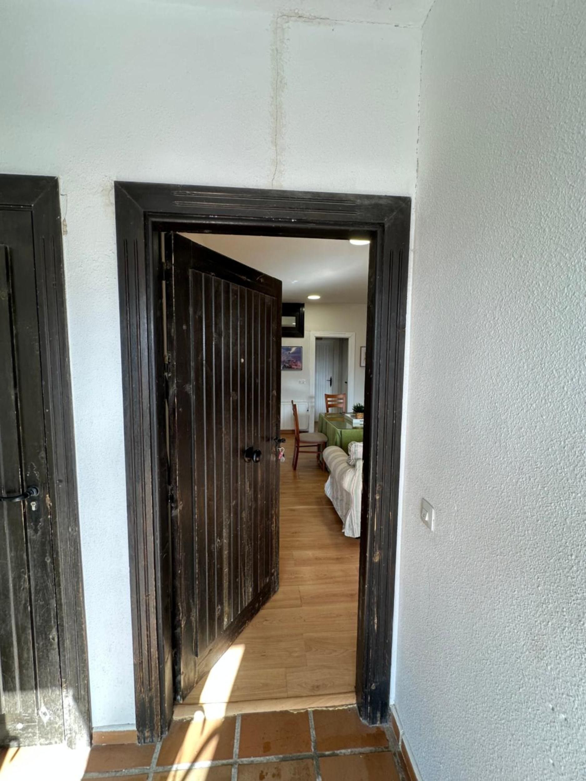 Un pasillo con una puerta de madera que da a una habitación con una cama y una mesa.