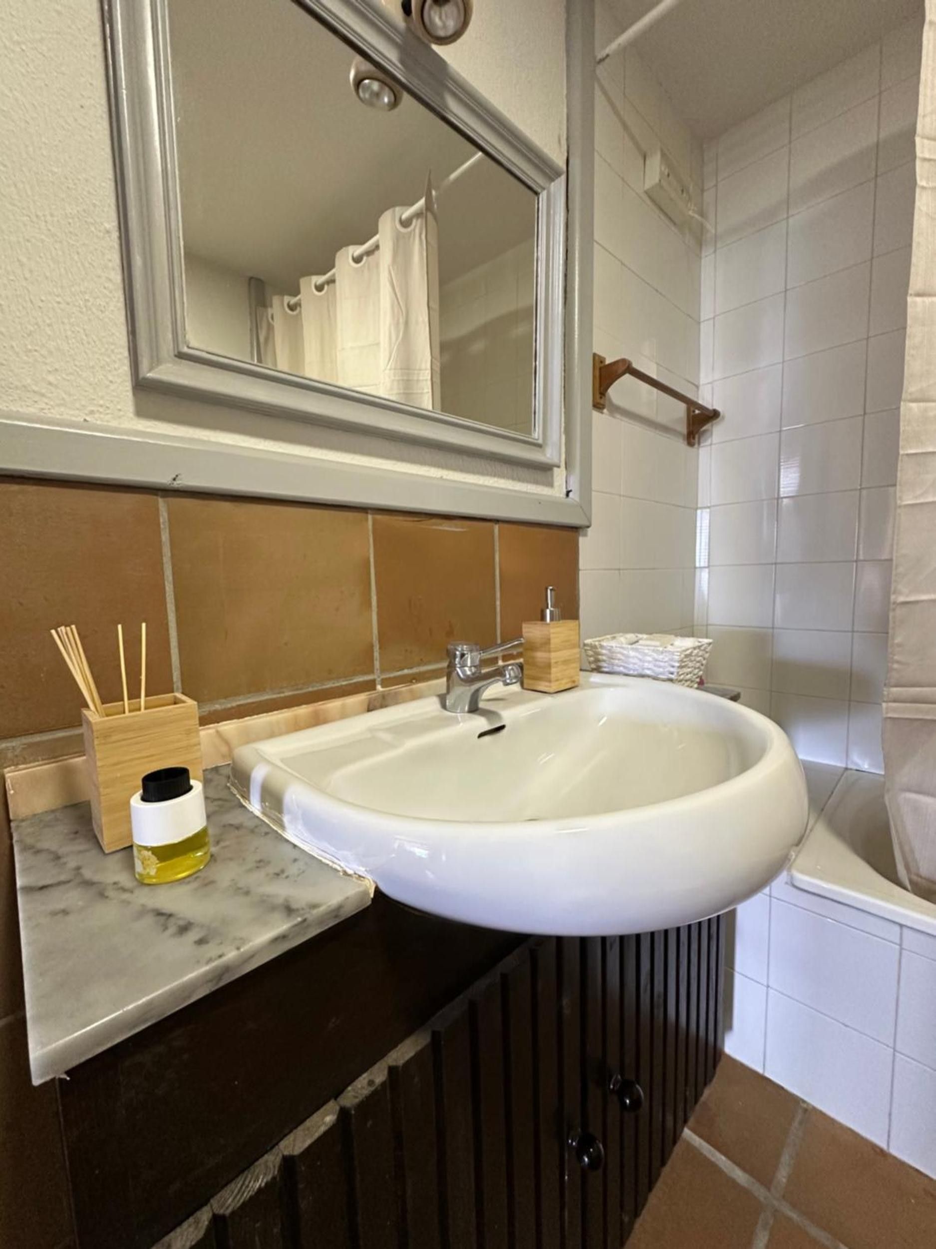 Un baño con lavamanos blanco, un espejo, un mueble de madera y una zona de ducha.