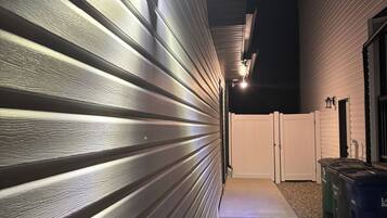 Un couloir avec un mur en métal et un chemin en béton menant à une zone délimitée par une grille.
