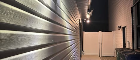Un pasillo con pared de metal y un camino de hormigón que conduce a una zona vallada.
