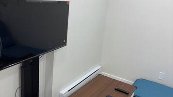 Une pièce comprenant un bureau, une chaise, un lit, un radiateur et un téléviseur fixé au mur.