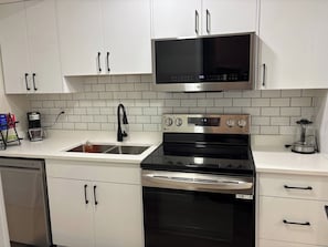 A kitchen with white cabinets, a black microwave, a stainless steel stove, and a coffee maker. - Cozy basement suite - home away from home (Saskatoon)